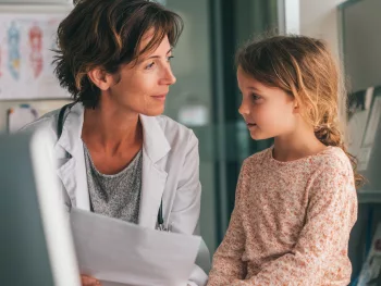 Médecin avec dans les mains le certificat médical MDPH à une petite fille lors d'une consultation