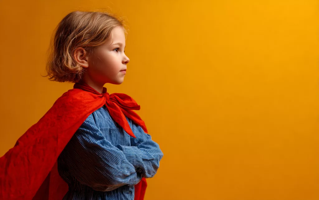 Enfant confiant portant une cape de super-héros rouge sur fond jaune, représentant l'estime de soi et l'empowerment des enfants avec troubles neurodéveloppementaux