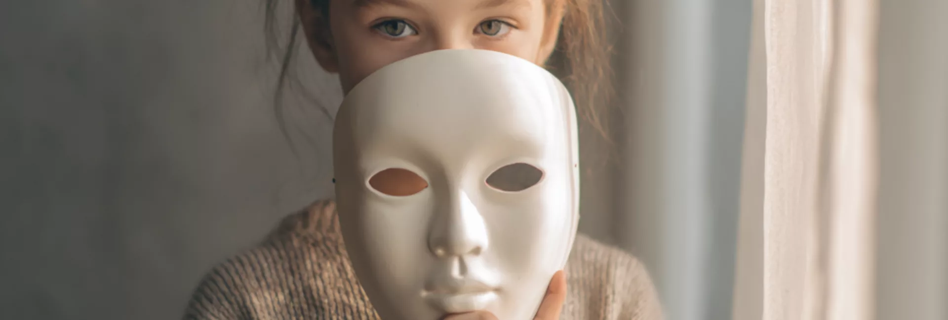 Fille autiste tenant un masque blanc devant son visage, regard sérieux, illustrant le camouflage des difficultés et des émotions vécues à l’école, dans une atmosphère calme et introspective. Filles autistes