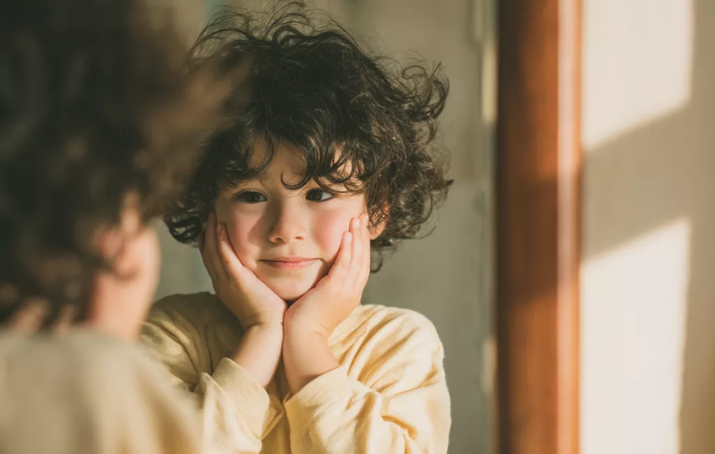 Enfant face à un miroir, testant des expressions du visage, illustrant le camouflage autistique.