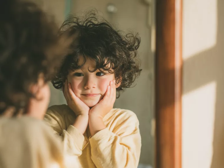 Enfant face à un miroir, testant des expressions du visage, illustrant le camouflage autistique.