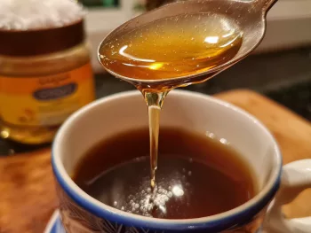 Cuillère de miel cru ou sirop d'agave coulant dans une tasse de café — remplacer le sucre par du miel dans son café