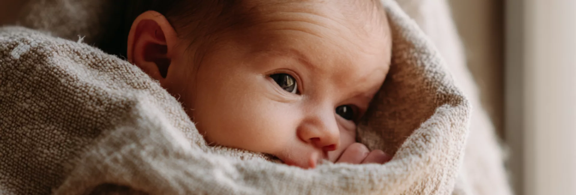 Nouveau-né blotti dans les bras de sa mère, le regard attentif — dès les premiers jours, bébé distingue le visage maternel à 20-30 cm