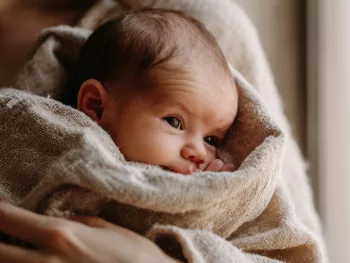 Nouveau-né blotti dans les bras de sa mère, le regard attentif — dès les premiers jours, bébé distingue le visage maternel à 20-30 cm