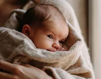 Nouveau-né blotti dans les bras de sa mère, le regard attentif — dès les premiers jours, bébé distingue le visage maternel à 20-30 cm