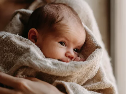 Nouveau-né blotti dans les bras de sa mère, le regard attentif — dès les premiers jours, bébé distingue le visage maternel à 20-30 cm