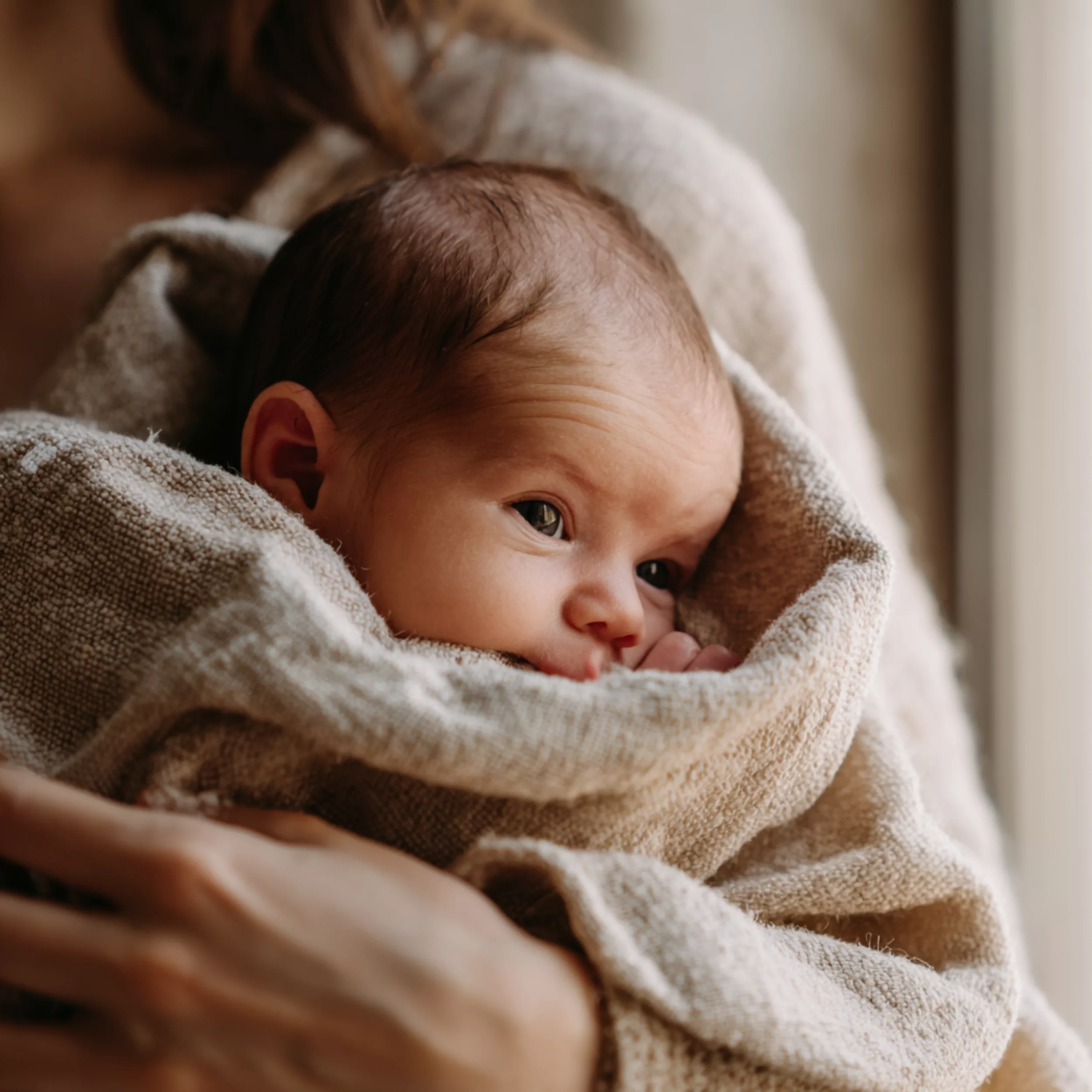 Nouveau-né blotti dans les bras de sa mère, le regard attentif — dès les premiers jours, bébé distingue le visage maternel à 20-30 cm