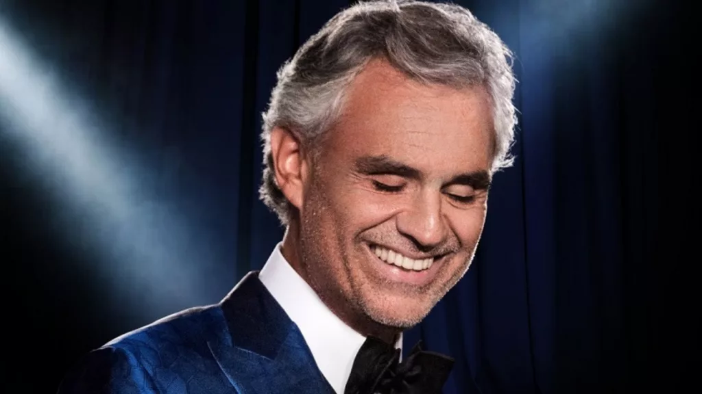 Andrea Bocelli, ténor italien aveugle depuis l'âge de 12 ans, souriant sur scène en costume bleu — plus de 90 millions d'albums vendus dans le monde