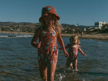 Deux jeunes enfants marchant seuls dans l'eau peu profonde au bord de la mer, illustrant l'importance de la surveillance pour prévenir les noyades.