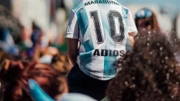 Enfant en maillot de foot argentin « Maradona 10 » sur les épaules d'un adulte, dans une foule ensoleillée.