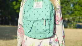 Enfant de dos portant un cartable turquoise dans un parc, image illustrant la rentrée scolaire et les dépenses liées aux fournitures. allocation de rentrée scolaire