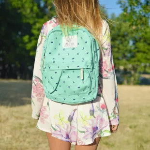 Enfant de dos portant un cartable turquoise dans un parc, image illustrant la rentrée scolaire et les dépenses liées aux fournitures. allocation de rentrée scolaire