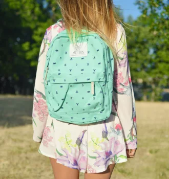 Enfant de dos portant un cartable turquoise dans un parc, image illustrant la rentrée scolaire et les dépenses liées aux fournitures. allocation de rentrée scolaire