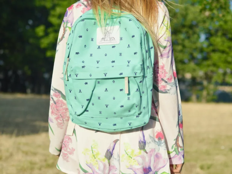 Enfant de dos portant un cartable turquoise dans un parc, image illustrant la rentrée scolaire et les dépenses liées aux fournitures. allocation de rentrée scolaire