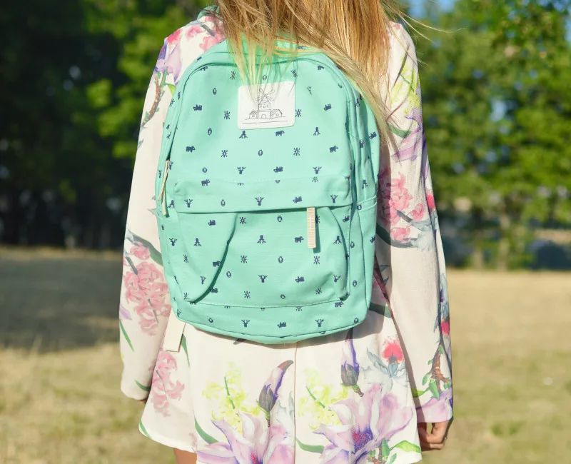 Enfant de dos portant un cartable turquoise dans un parc, image illustrant la rentrée scolaire et les dépenses liées aux fournitures. allocation de rentrée scolaire