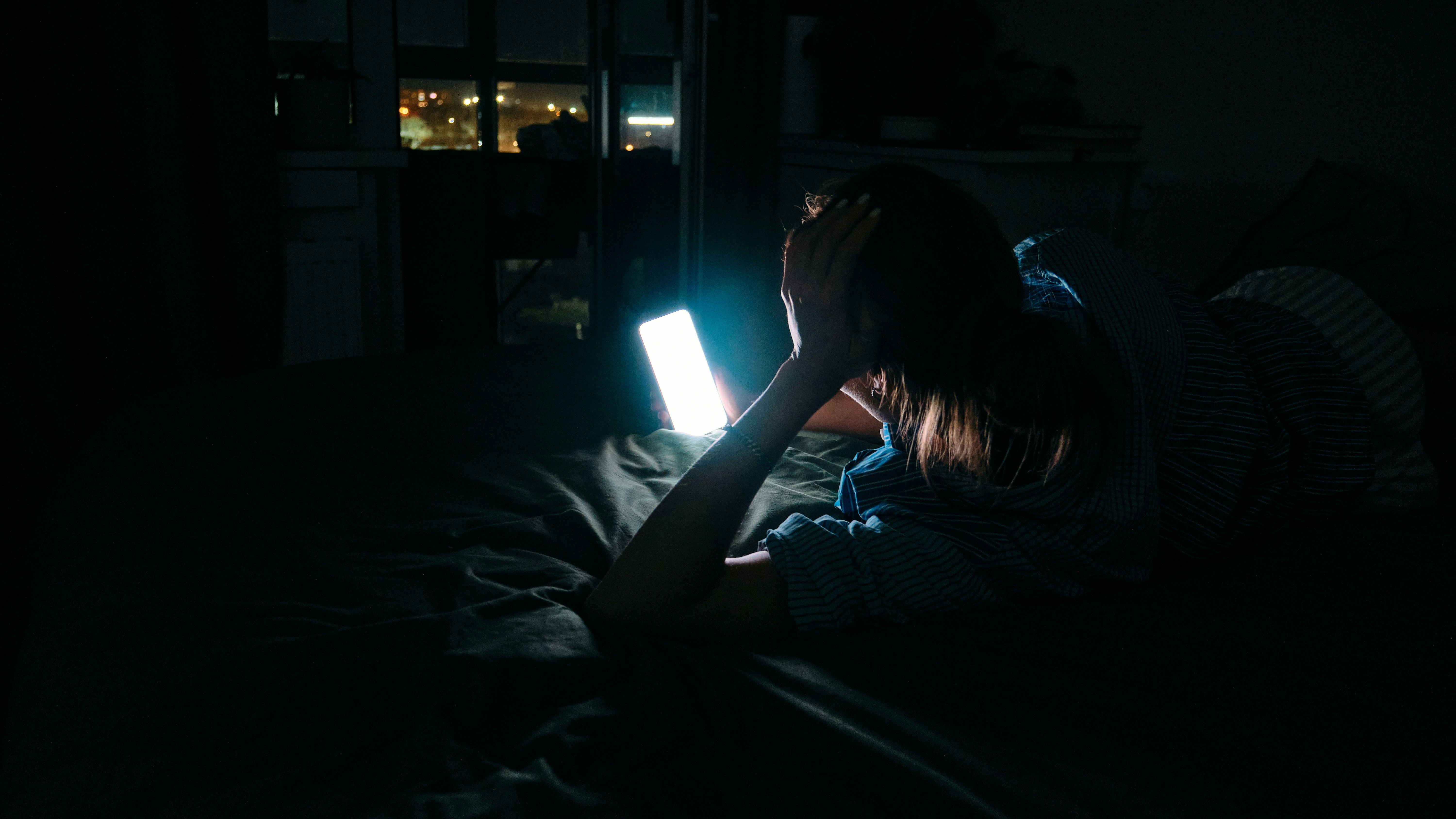 Porter plainte pour harcèlement scolaire : une personne allongée sur son lit dans le noir, la main sur la tête, éclairée par l’écran de son téléphone